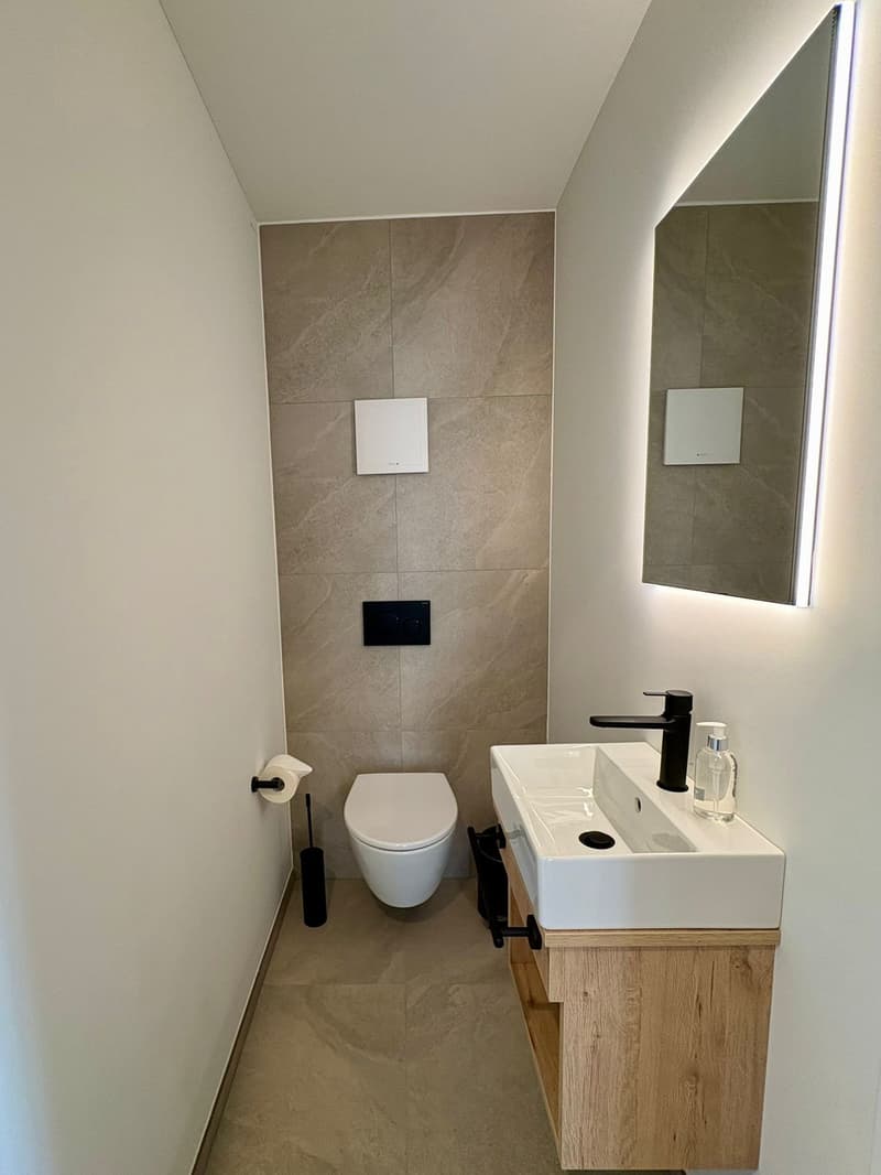 a small bathroom with a toilet, a sink, and a mirror with a lit frame