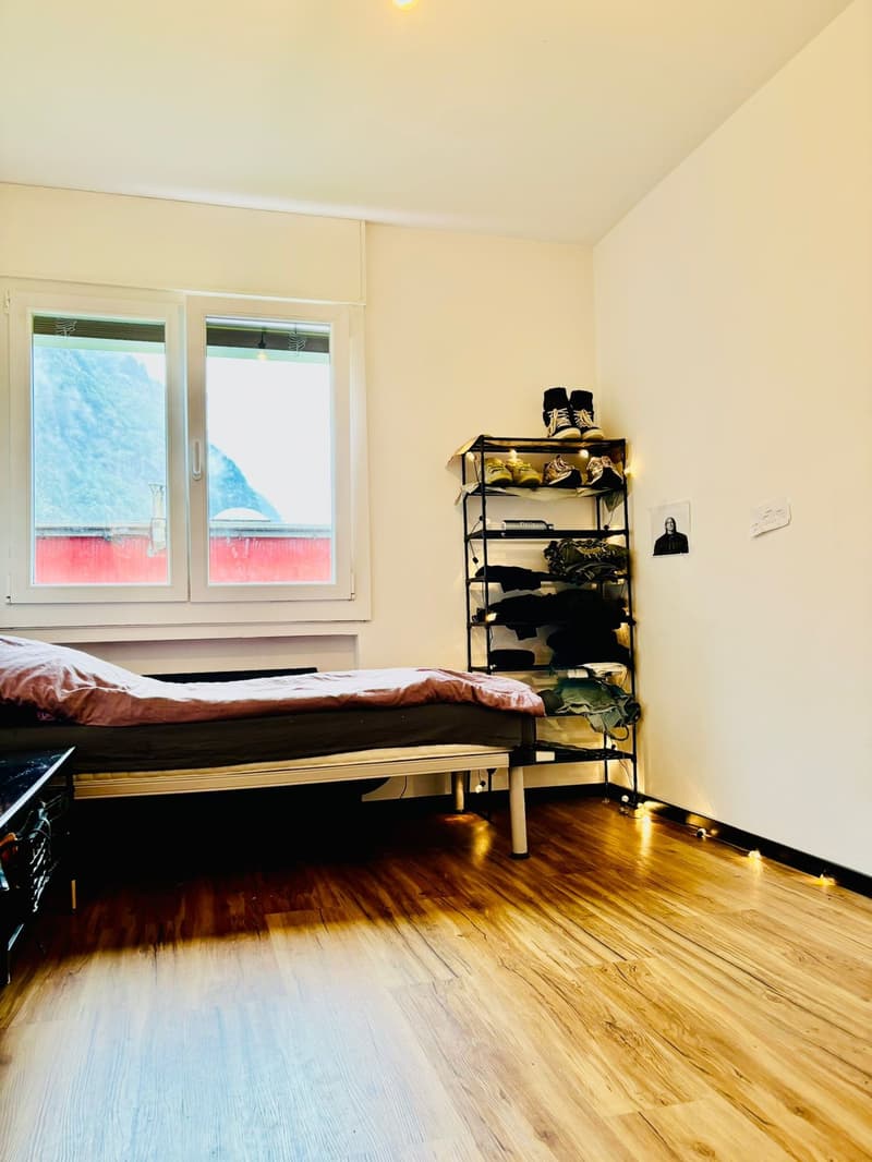 single bed, wooden floor, large windows, shelf with shoes and clothes, picture on wall