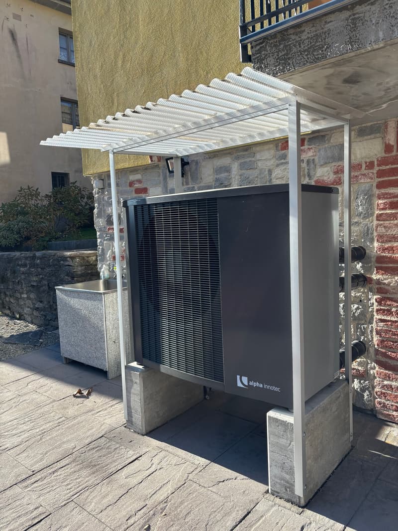 An outdoor area with a metal structure housing an air conditioning unit, a stone wall, and a concrete floor.