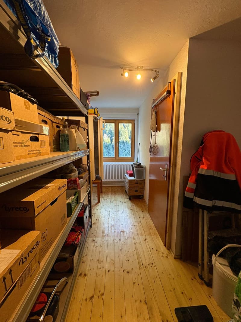 Corridor with wooden floor, shelves with boxes, open door, window, radiator, storage box, orange jacket, trash bin