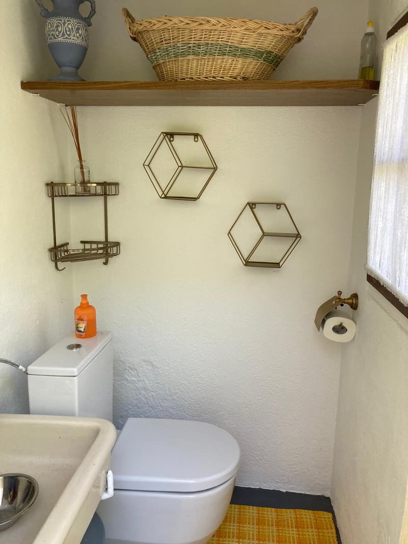 Bathroom with white toilet, sink, and shelves with decorative items