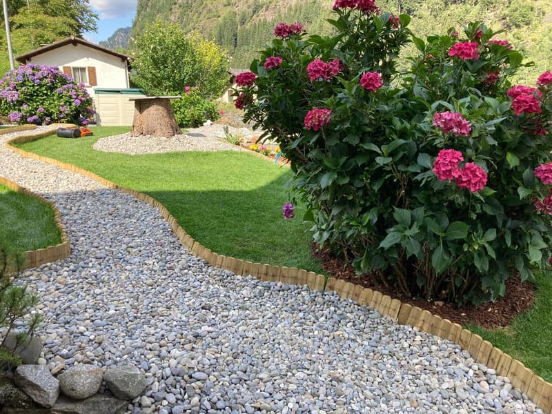 gravel pathway, green lawn, flower beds, wooden fence, mountain view