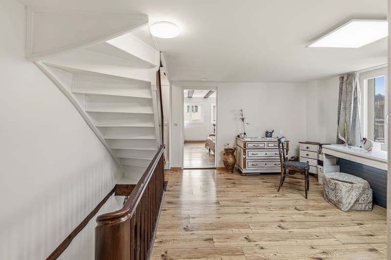 wooden floor, white walls, white staircase, wooden handrail, white ceiling, white ceiling light, white desk, chair, vase, drawers, window with curtains
