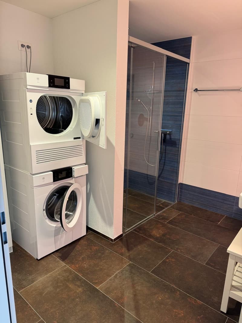 Laundry room with stacked washing machine and dryer, glass shower enclosure, tiled floor