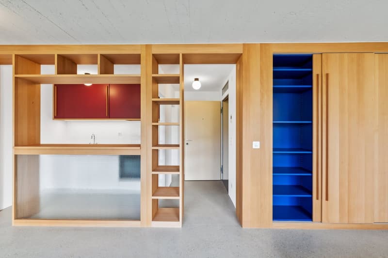 modern kitchen with wooden cabinets, glass partition, red cabinets, blue shelves, white door, white walls, gray floor