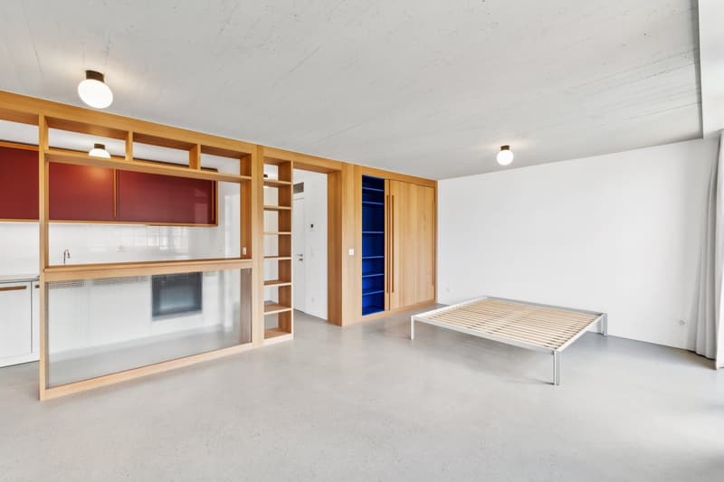 Empty room with wooden built-in cabinets, white walls, gray floor, and a bed frame.