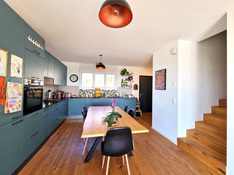 kitchen with dining area, wooden floor, wooden dining table, black chairs, blue cabinets, white walls, ceiling lamps, staircase