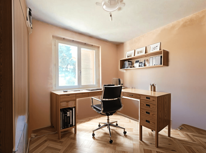 A room with a wooden desk, a black office chair, a window, and a shelf with picture frames and books.