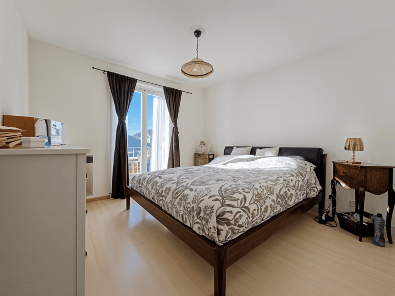 wooden bed, floral bedspread, bedside tables, lamps, curtains, wooden floor, white walls, window with view