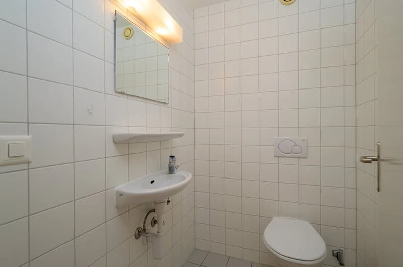 small bathroom with white tiles, sink, mirror, toilet, light