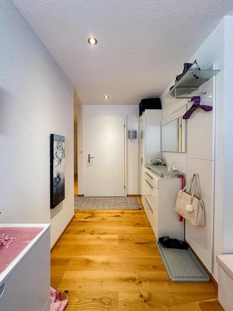 Long corridor with wooden floors, white walls, closet, and entrance to a room.