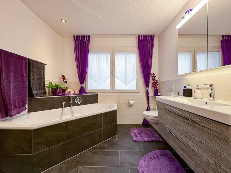 large bathtub, separate shower, double sink, mirrored vanity, toilet, shelves above vanity, purple curtains, towel racks