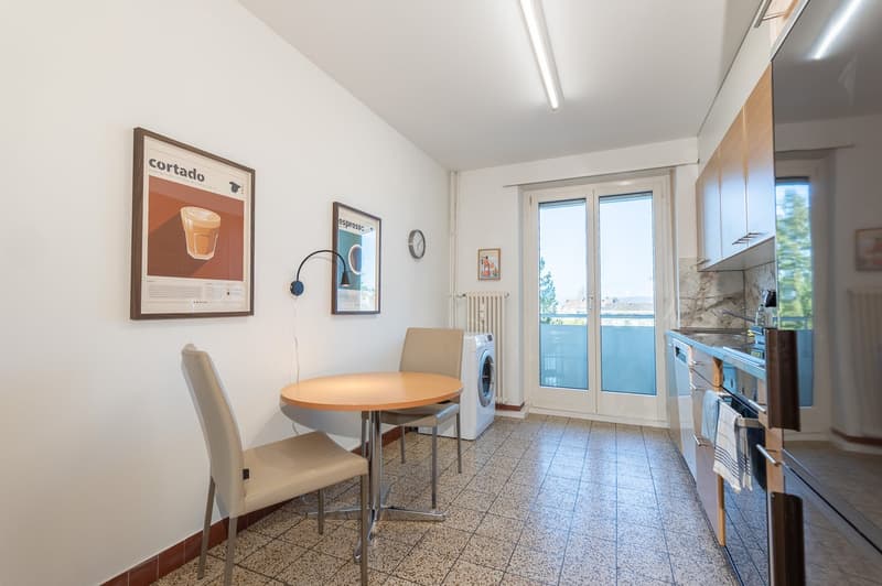 modern kitchen, tiled floor, white walls, small table and chairs, washing machine, sink, oven, refrigerator, glass door leading to balcony