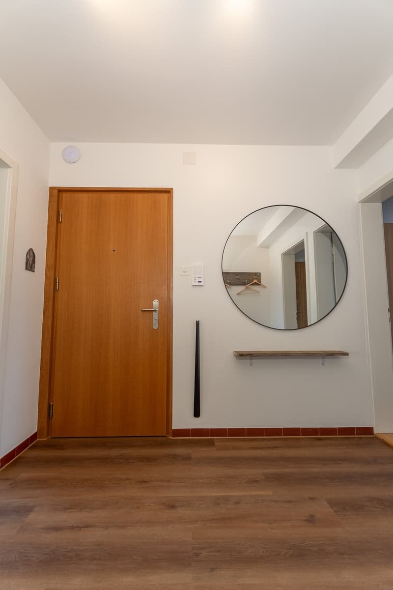 white walls, wooden floor, wooden door, mirror with wall hanger, empty room