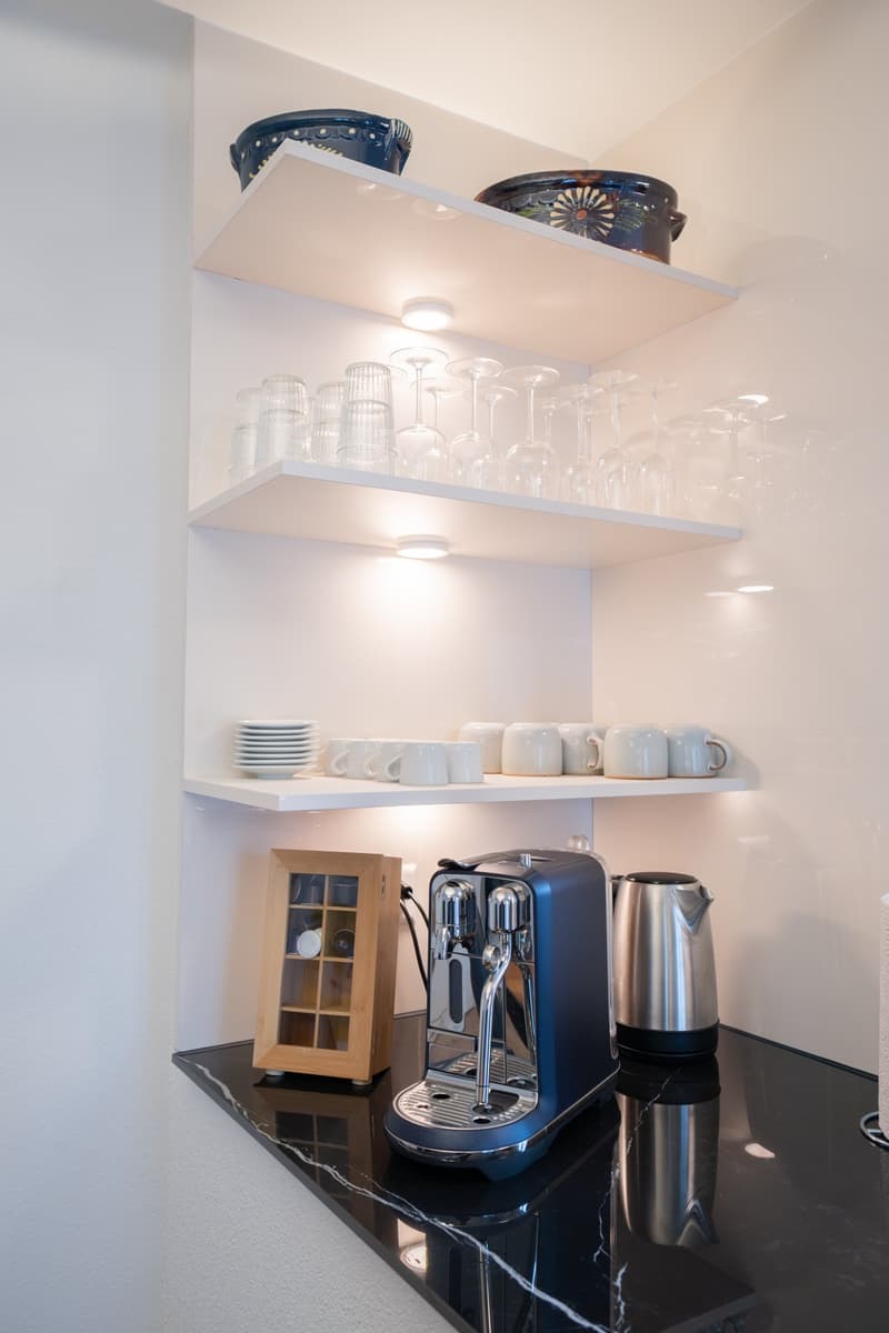 Modern kitchen with open shelving, coffee maker, kettle, and dishwasher on a black marble countertop