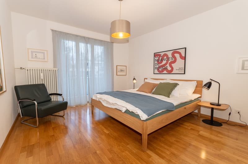 Single bed, bedside table with lamp, armchair, curtains, picture frames, lamp, wall outlet, radiator