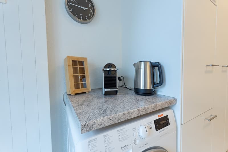 Laundry room with marble countertop, clock, and appliances including a washing machine, coffee maker, and kettle.