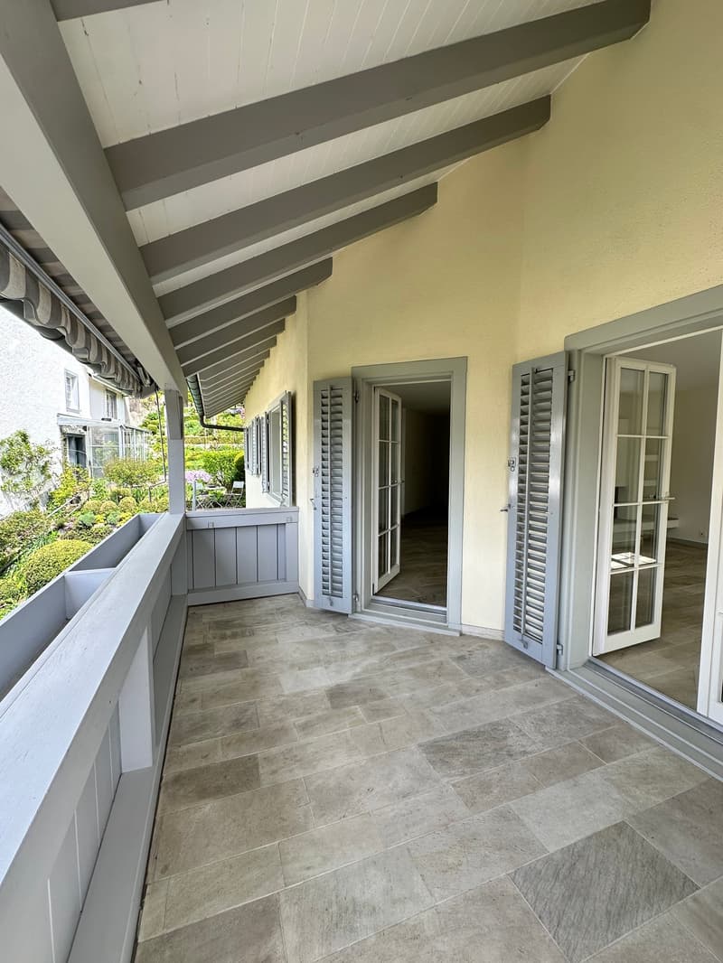 large balcony, tiled floor, white walls, wooden ceiling, glass doors, white shutters