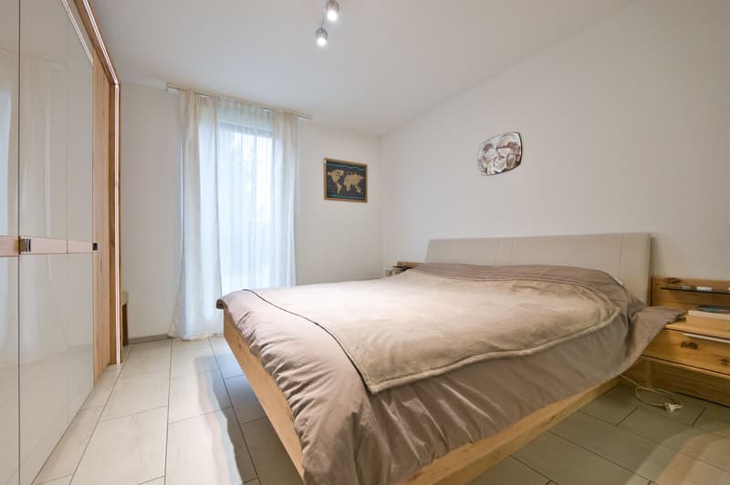 Spacious bedroom with wooden floor, large bed, bedside tables, wall decorations, window with curtains, and built-in wardrobe.