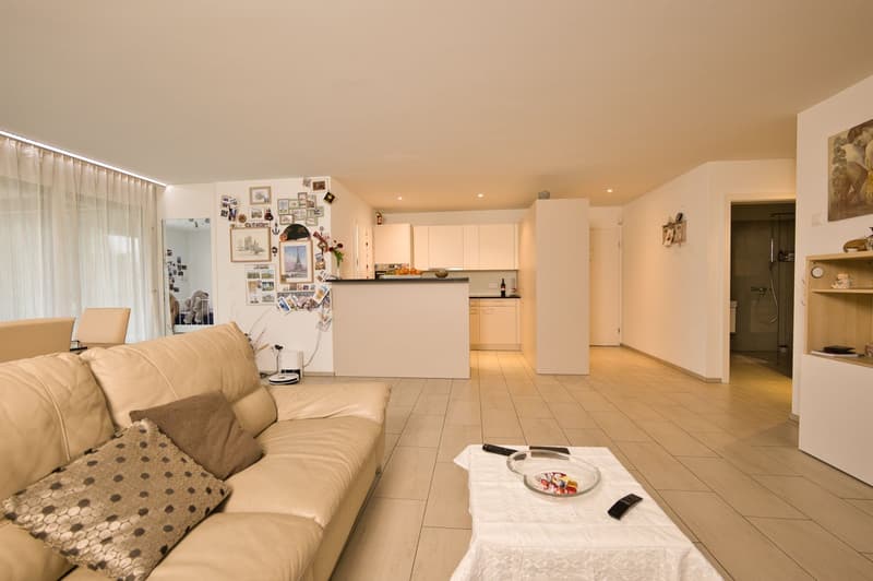 Open layout living room, beige leather sofa, center table, kitchen with bar countertop, white cabinetry