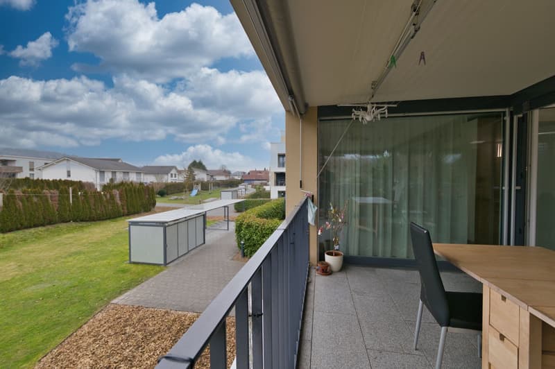 Balcony with table and chairs, a large window with curtains, plants, grass lawn