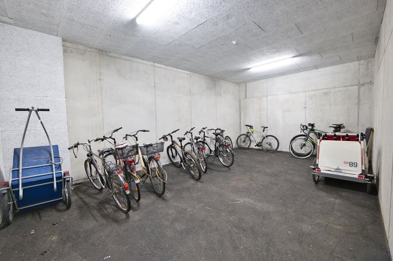 A concrete garage, several bicycles are parked in a row, and a carriage in the corner.