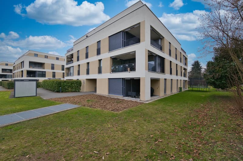 Three story apartment building, balcony on each floor, grey and beige exterior, fenced yard