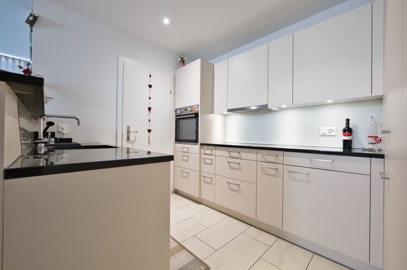 modern white kitchen, granite countertop, white cabinets, black trim, stainless steel sink, faucet, electric kettle, modern oven, dishwasher, wine bottle, floor tiles