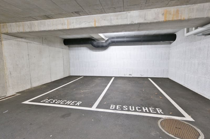 Underground parking area with concrete walls and floors, two parking spaces with 'BESUCHER' written on the ground.
