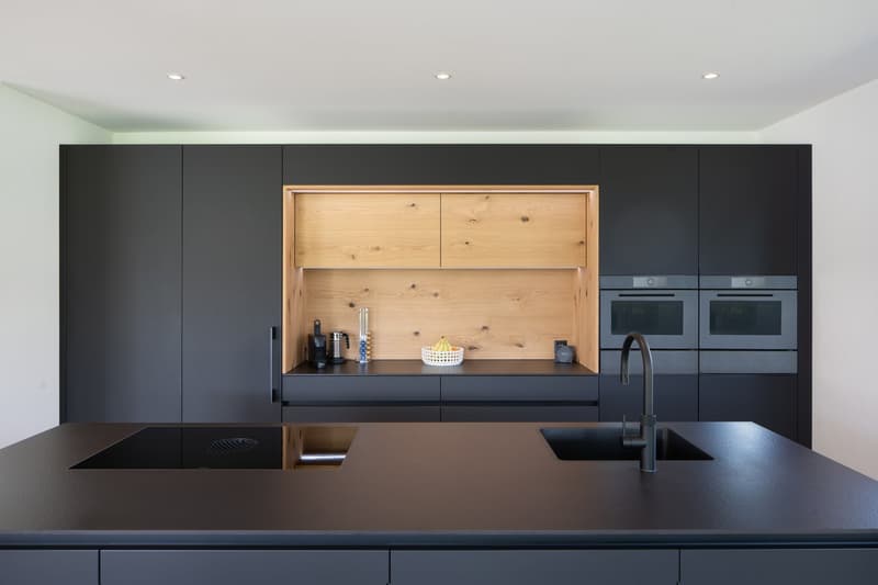 modern kitchen with black countertops, wooden cabinets, black appliances, wooden shelf, sink, faucet, induction cooktop
