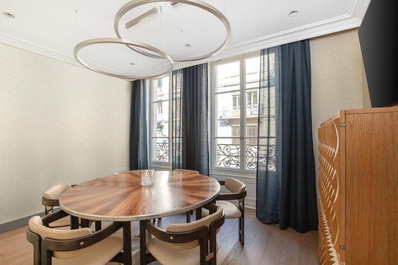 Spacious dining room with a round wooden dining table and chairs, large windows with decorative wrought-iron balconies, and modern circular pendant lighting fixtures.