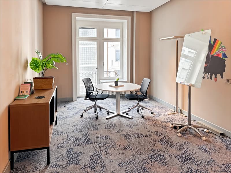 Office with beige walls, round table, two chairs, wooden cabinet, potted plant, whiteboard