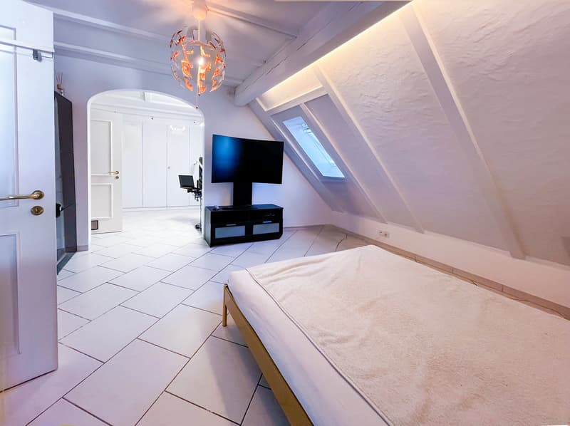 Bedroom with white tiled floor, bed, TV, cabinet, and chandelier