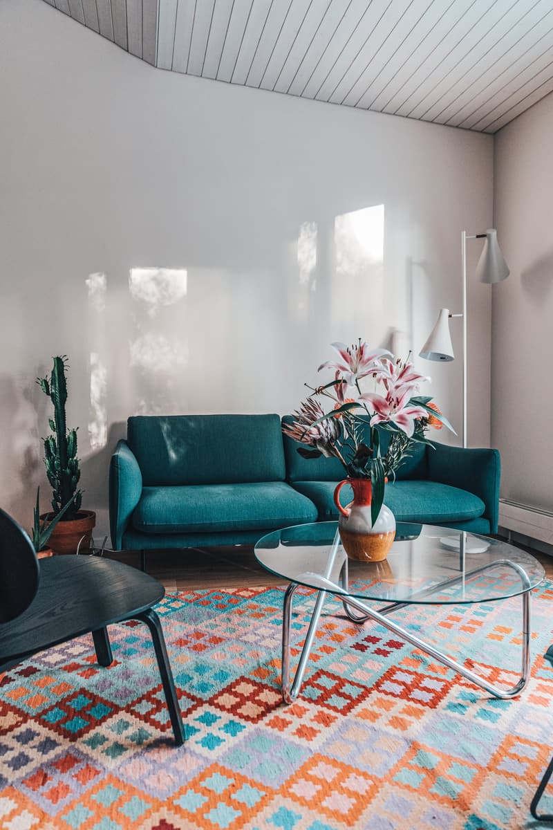 teal couch, glass table, vase, geometric rug, standing lamp, cactus plant