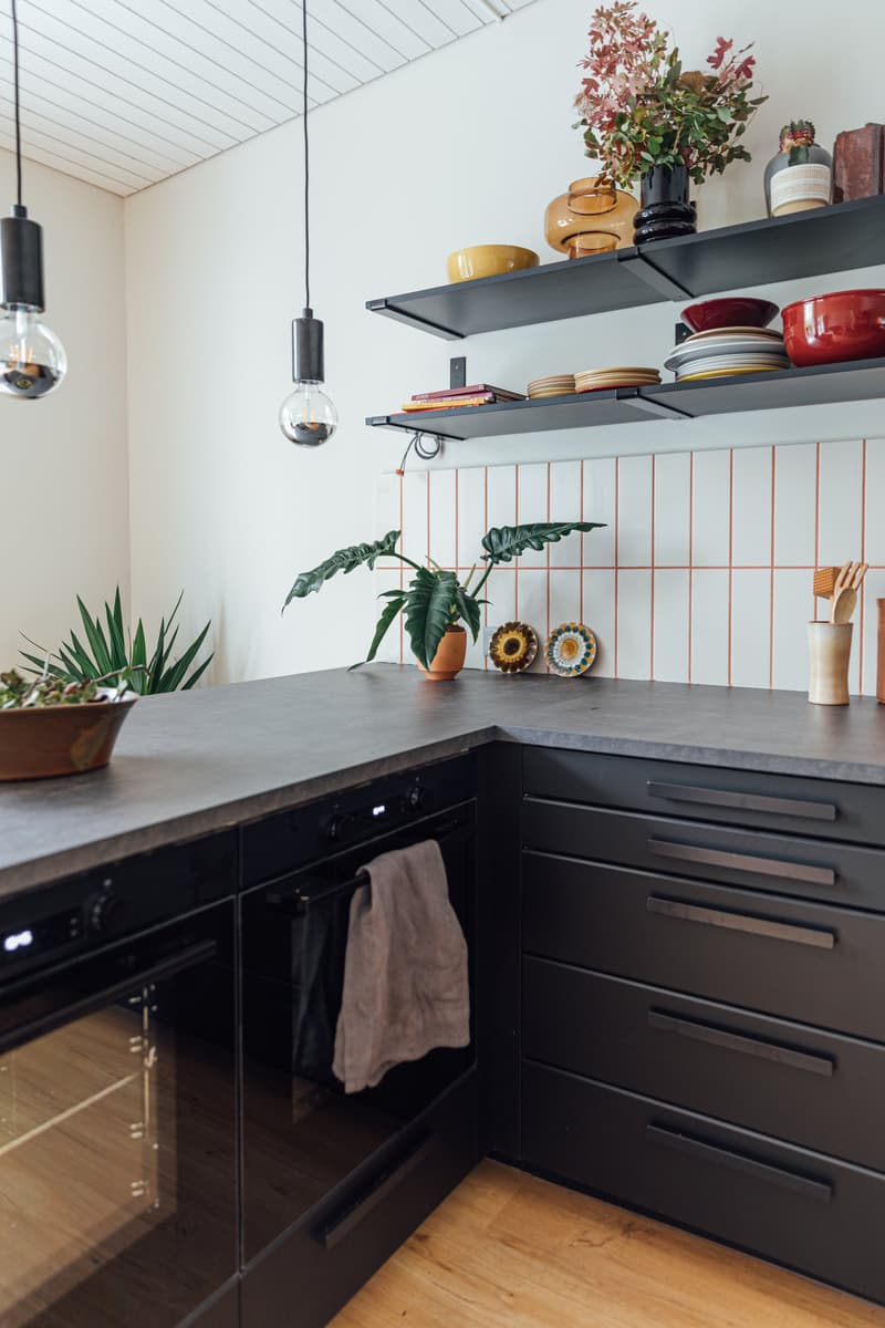 modern kitchen with gray countertop, black cabinets, two-level shelves with assorted items, plants on the countertop, black oven with glass door