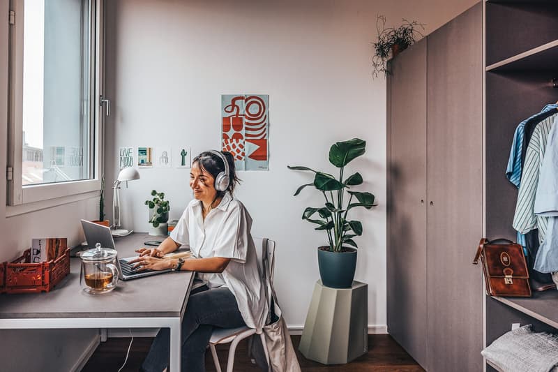 desk with laptop, chair, headphones, potted plants, wardrobe, window, books, lamp