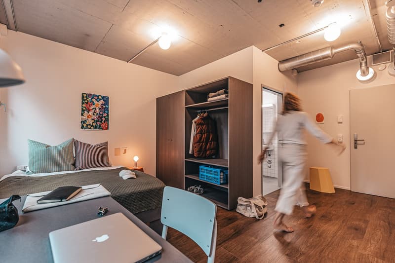 single bed, nightstand, desk with laptop, chair, closet, artwork, lamps