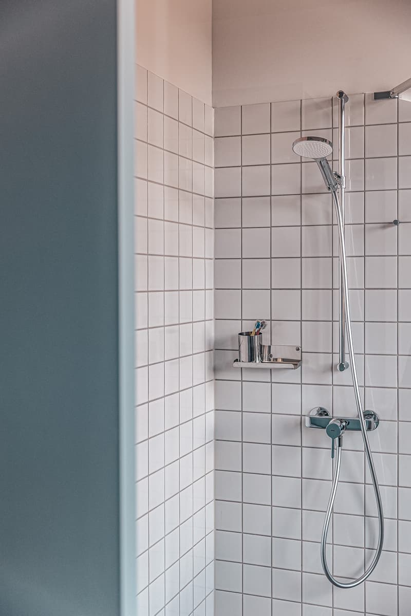 tiled wall, silver shower head, metal tray with toothbrush holder, metal soap dish
