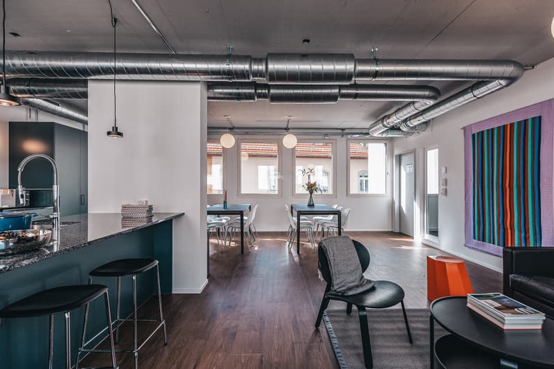 modern kitchen with granite countertops, pendant lighting, dining area with tables and chairs, wooden floor, black sofa, coffee table, colorful wall hanging