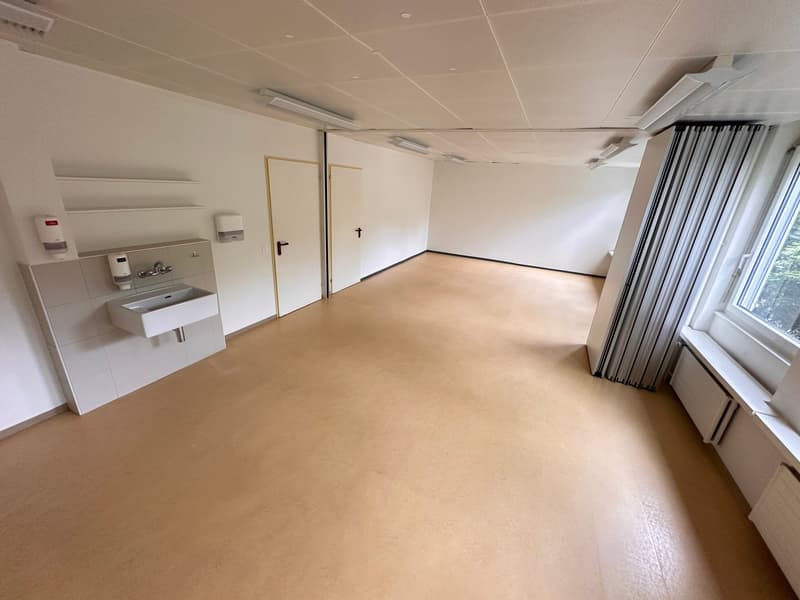 Empty room with tan floor, white walls, open door, sink with faucet, and a window with curtains