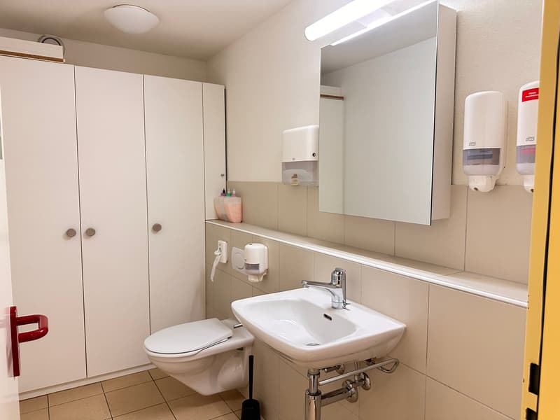 Modern bathroom with white tiles, a toilet, sink, mirror, and hand soap dispensers