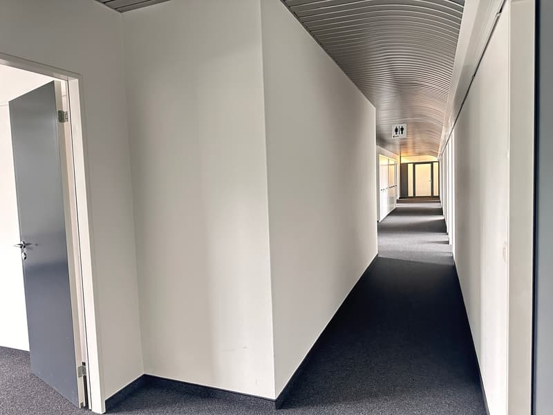 Empty white hallway with gray flooring and high ceiling