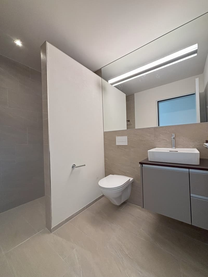 modern bathroom with white tiles, white toilet, white sink, mirror, and a window