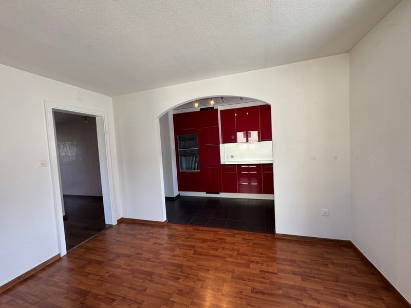 Empty room with wooden floor, white walls, arched doorway, red kitchen cabinets, black tiled floor, ceiling lights