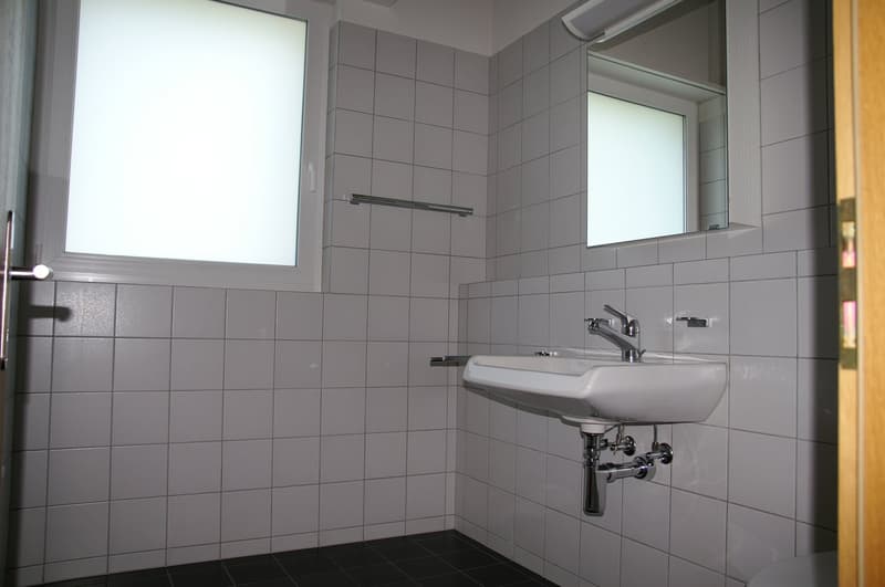 Bathroom with white tiles, white sink, silver faucet, mirror, window, and a wooden door.
