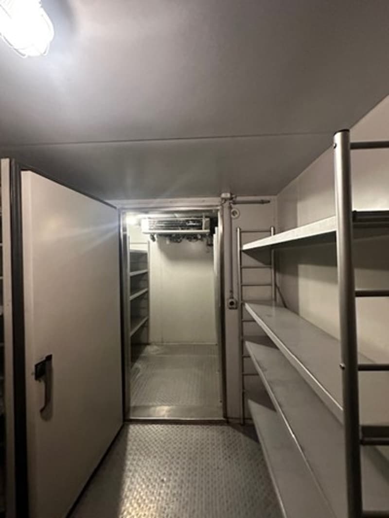 Small room, metal shelves, metal flooring, open door, air vent on the ceiling.