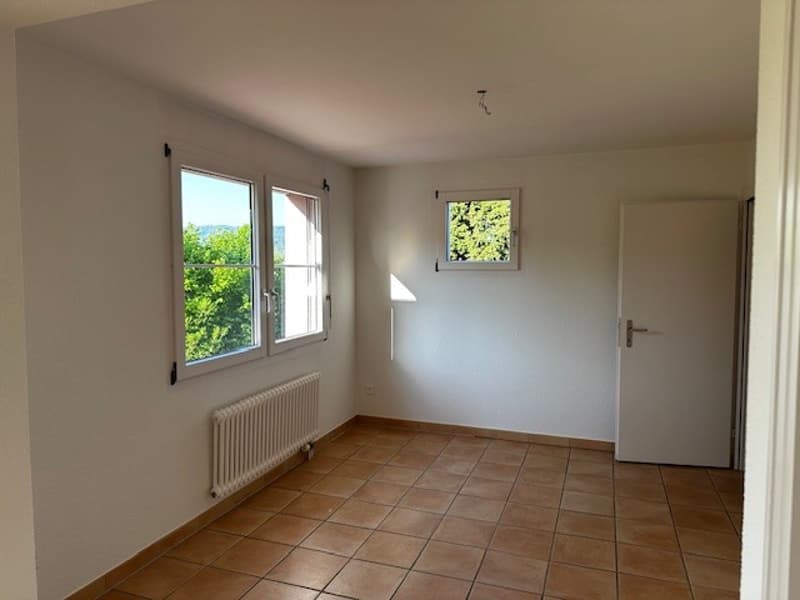 empty room with white walls, brown tiles, two windows, white door, white radiator