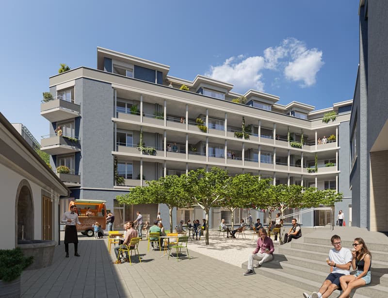 Multi-story apartment building with balconies, surrounded by trees and a public plaza with people sitting and socializing. The building has a modern, gray and white facade with large windows.