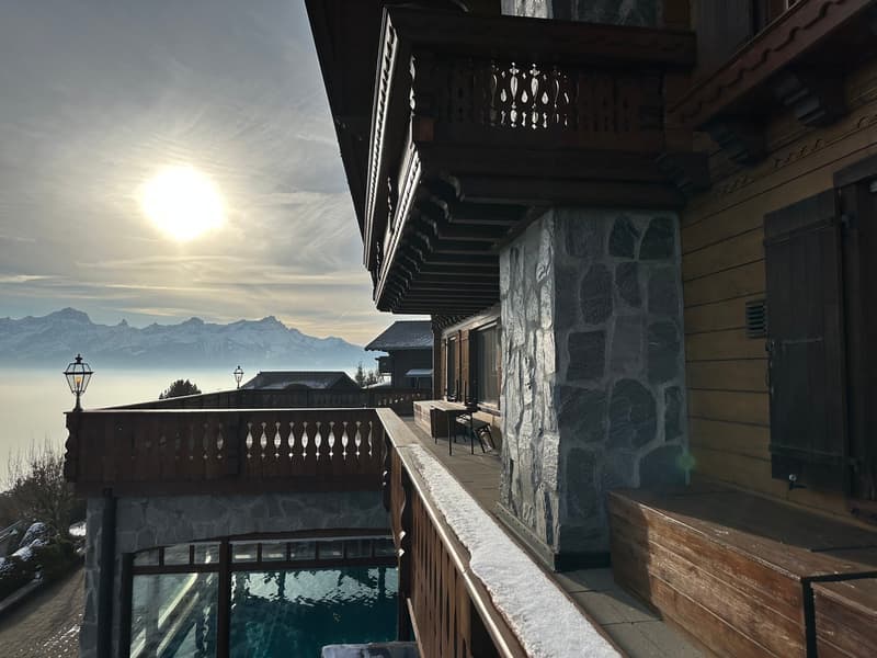 balcony, stone wall, swimming pool, mountain view, wooden table and chairs, lamp