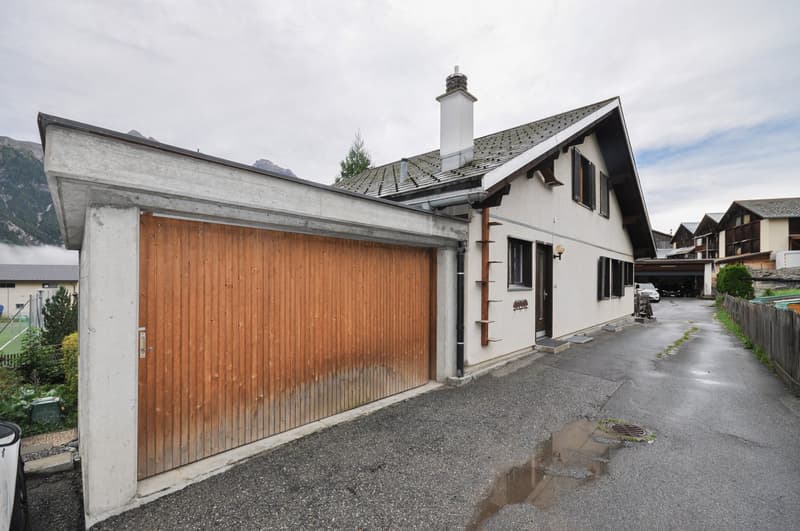 Facade with large wooden garage door, white exterior, small windows, chimney, gray gravel driveway